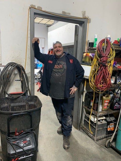 A man is leaning against a door in a garag | Franklin Transmission and Auto Care