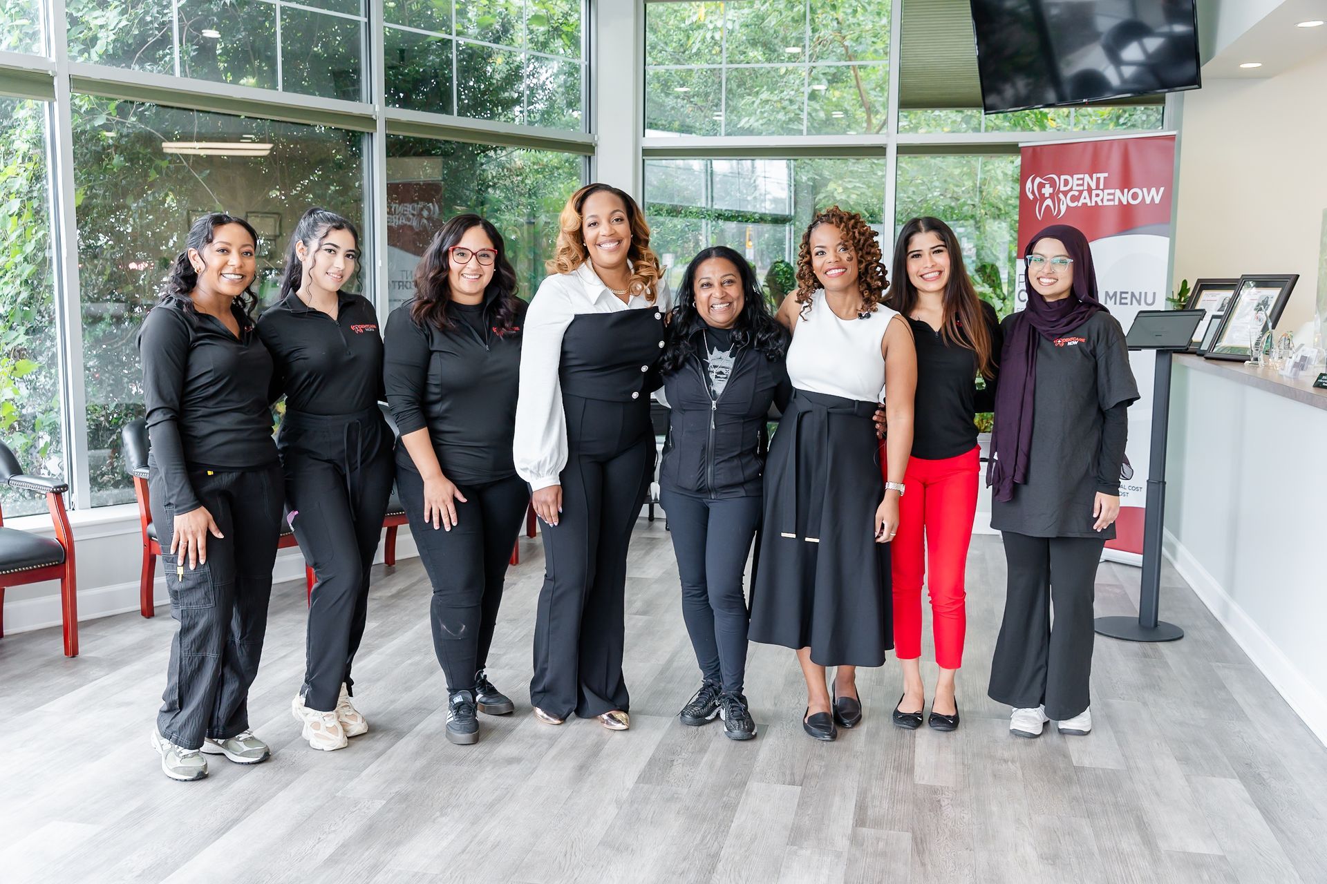 A group of eight people stand together in a well-lit lobby, smiling and dressed in professional attire.