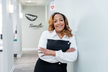Dr. Dominique Bonner stands with crossed arms in a dental office hallway near a sign that says Smile.