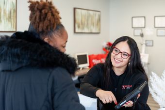 A person smiling while showing a digital tablet to a client at a reception desk.