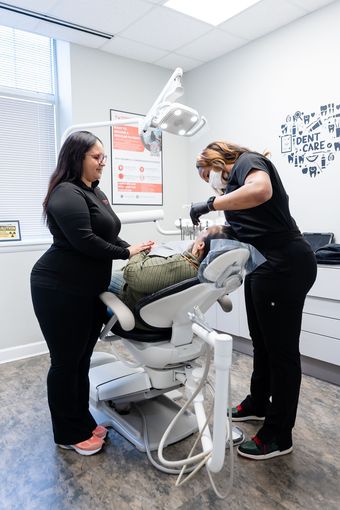 Two dental professionals in a clinic treat a patient lying in a reclined chair.