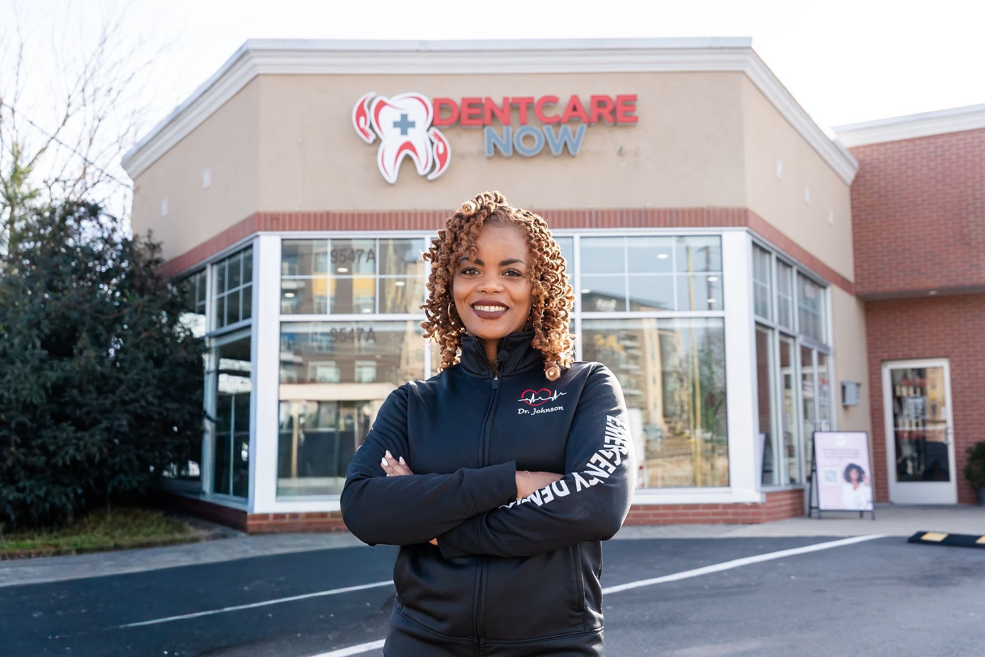 Dr. Rasheeda Johnson stands with arms crossed in front of a DentCare Now dental office building.