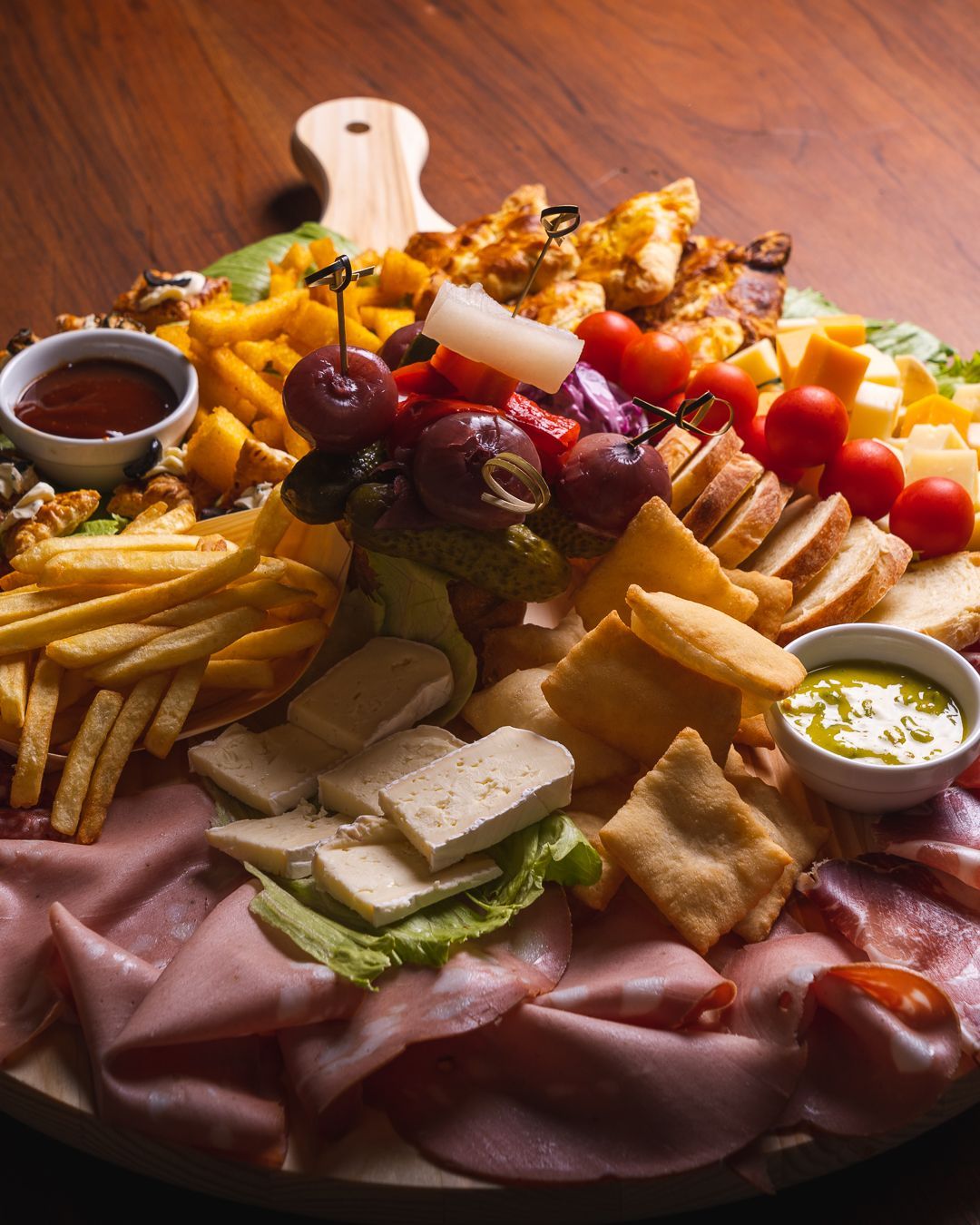 Tagliere di salumi con carni, formaggi, frutta, verdura e salse su una superficie di legno.