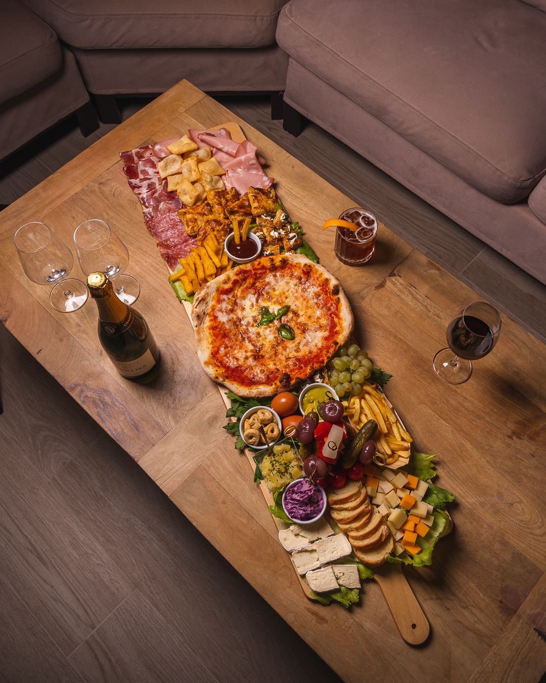 Vassoio di legno con salumi, pizza e antipasti su un tavolo, con vino e bevande.