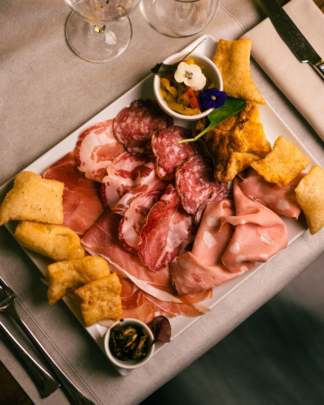 Tagliere di salumi su un piatto bianco con carne, pane fritto e salse.