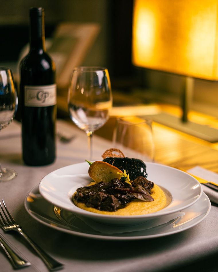 Cena elegante: brasato di carne su polenta, con vino e bicchieri sul tavolo.