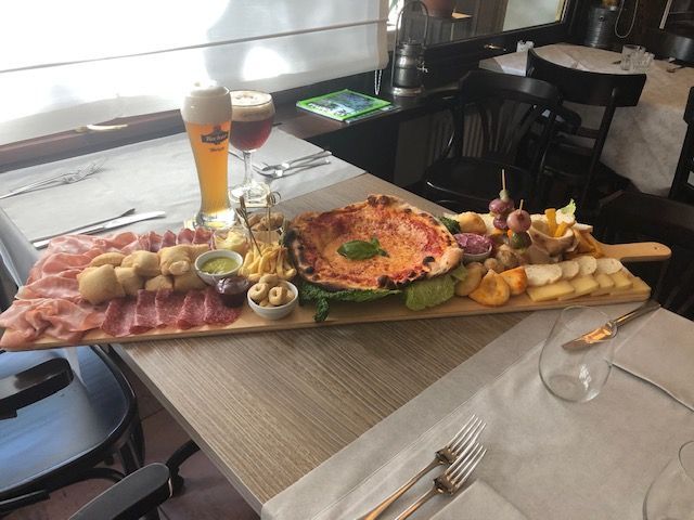 Grande tagliere di legno con pizza, salumi, formaggi, snack e bicchieri di birra su un tavolo di un ristorante.