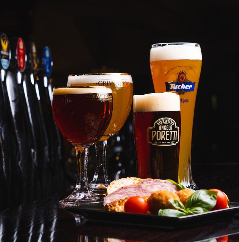 Bicchieri di birra, scura e chiara, con cibo su un vassoio nero su uno sfondo scuro, vicino ai rubinetti della birra.