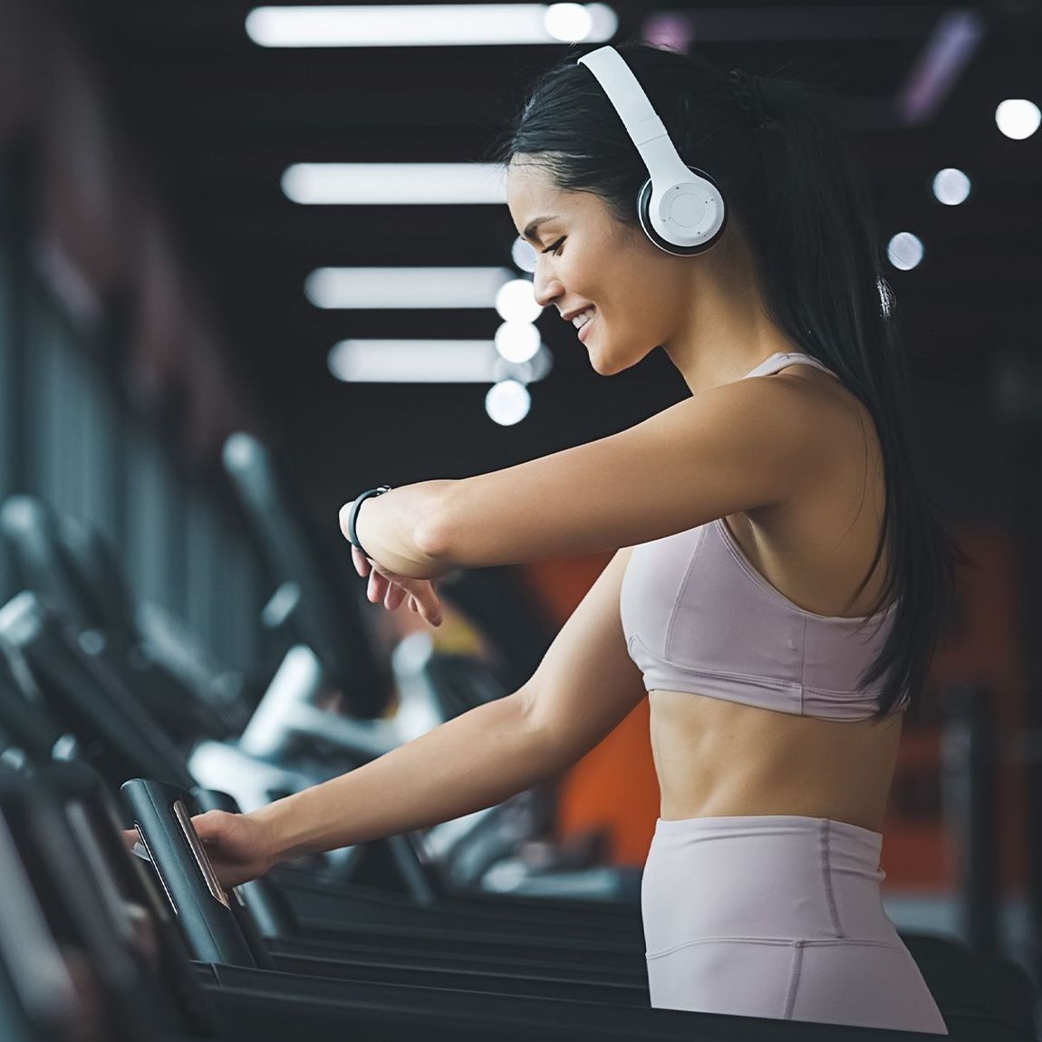 A girl is working out in the fitness center, wearing white headphones.
