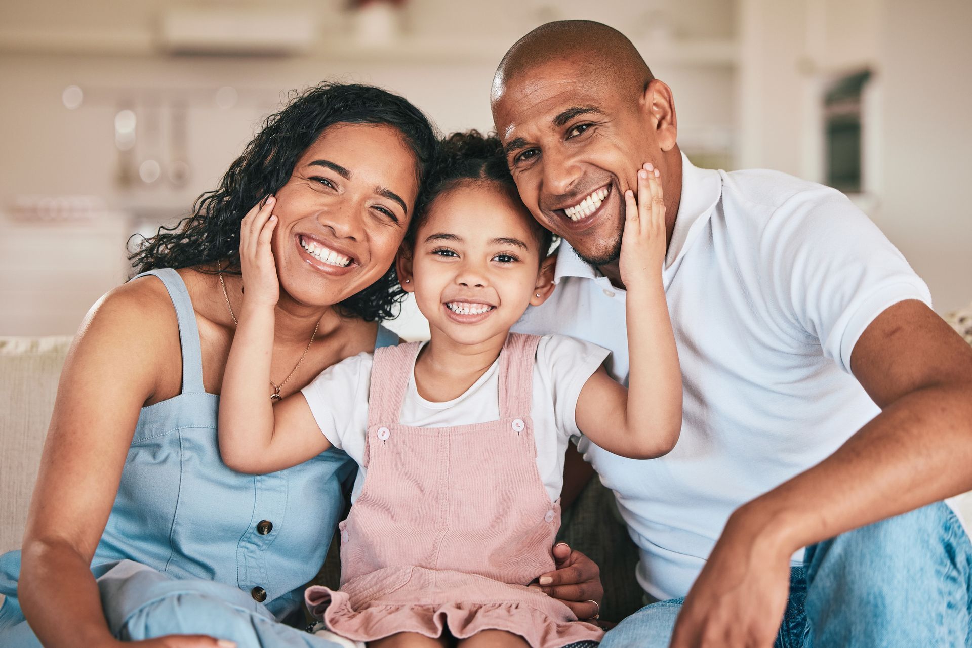 Family of three smiling, posing for photo: mother, father, and young daughter.