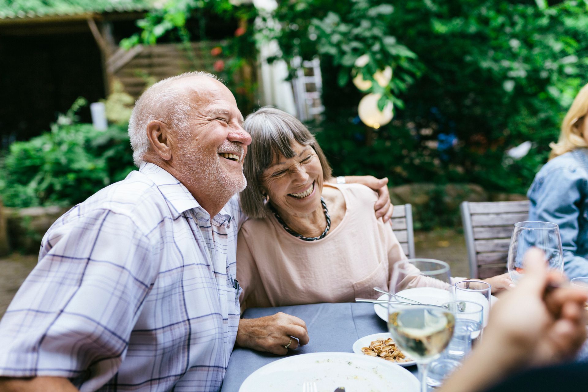 Smiling elderly couple at an outdoor table, man's arm around the woman.