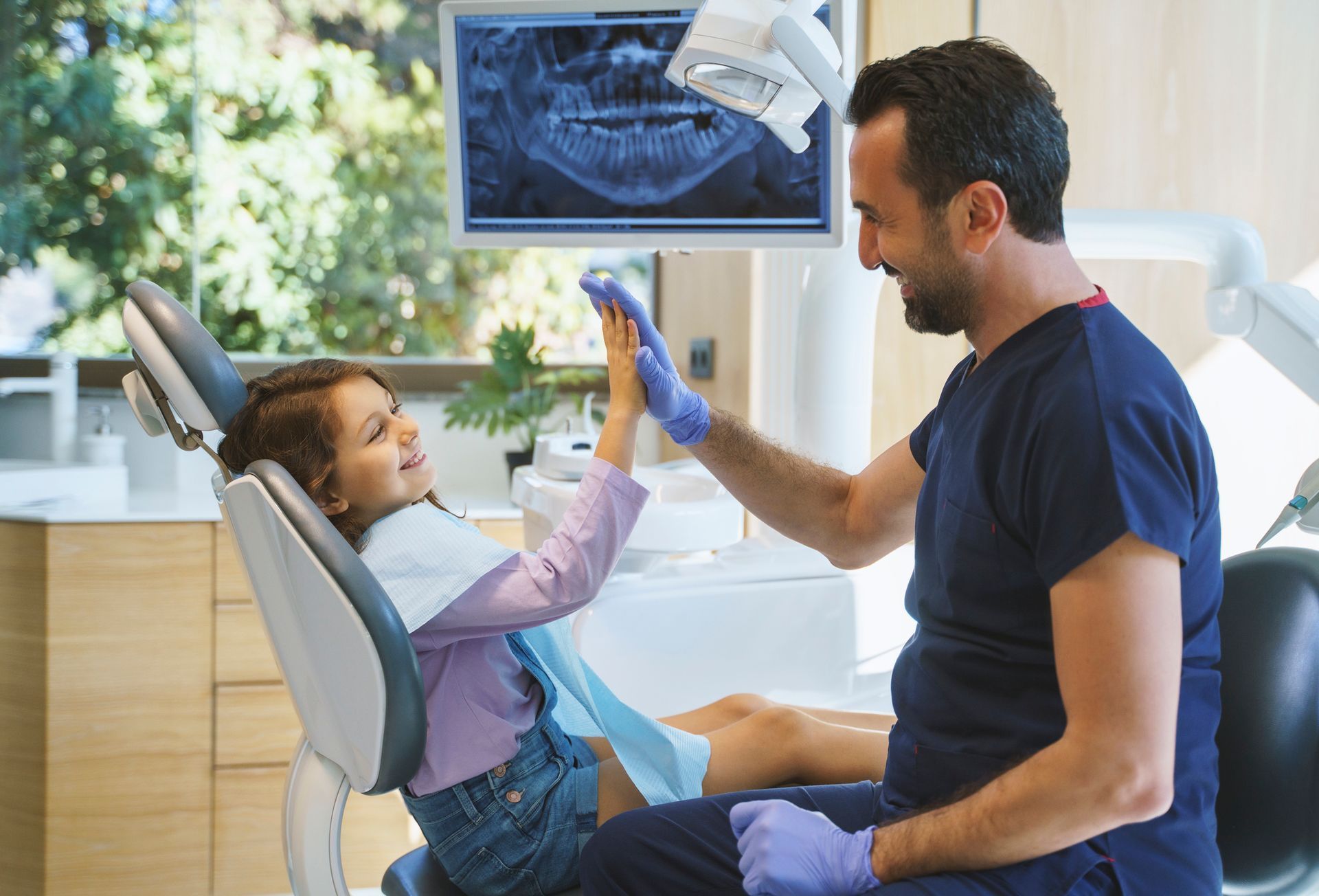 Dentist giving a high five to a young girl in a dental chair after a successful check-up.