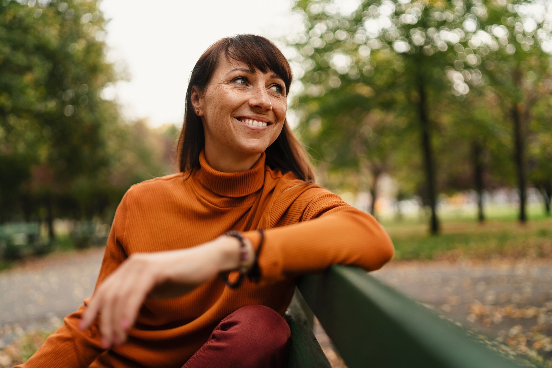 Girl with curly blonde hair smiles widely, eyes closed, in front of a green, leafy background.