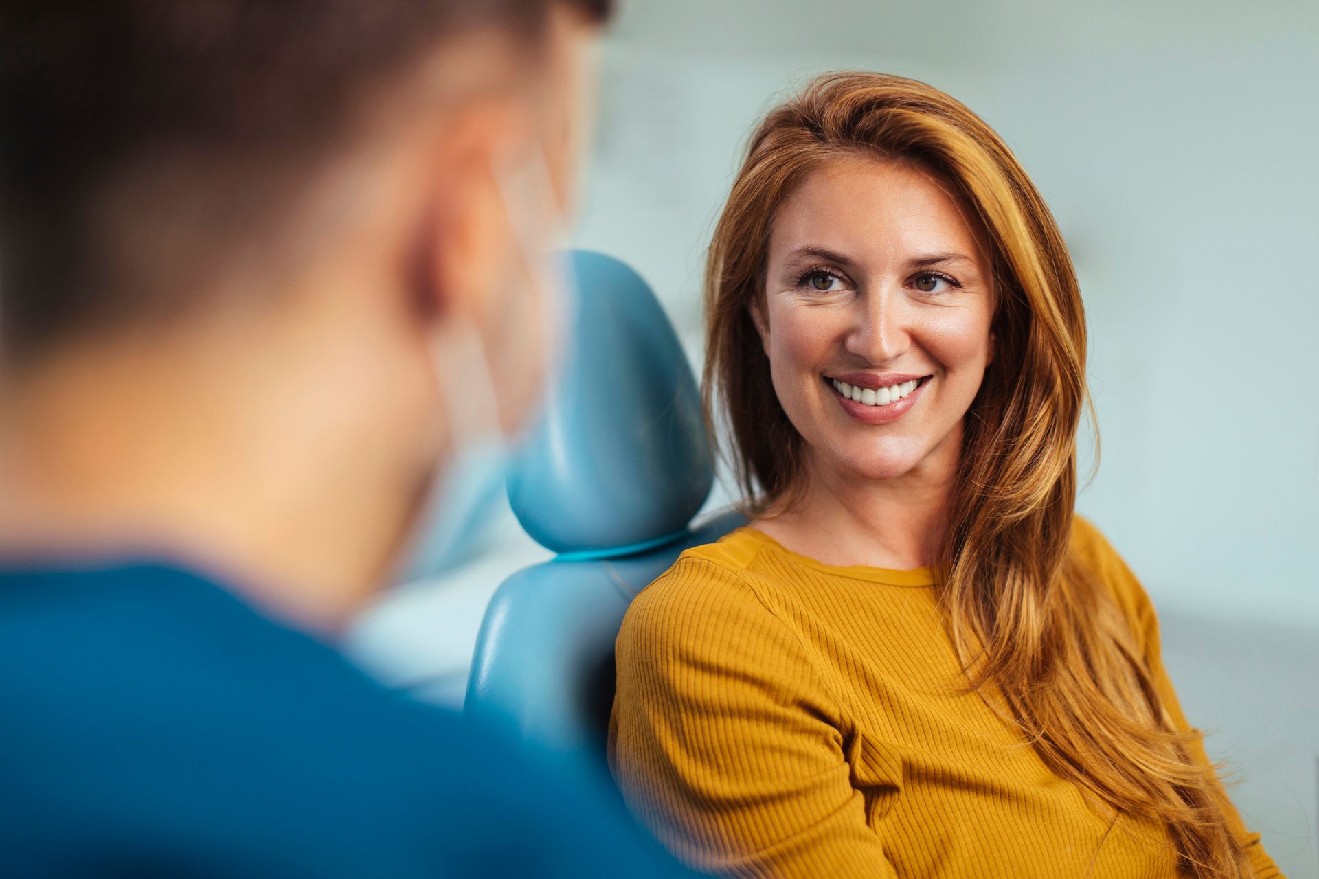Woman with red hair smiles at dentist in dental chair.