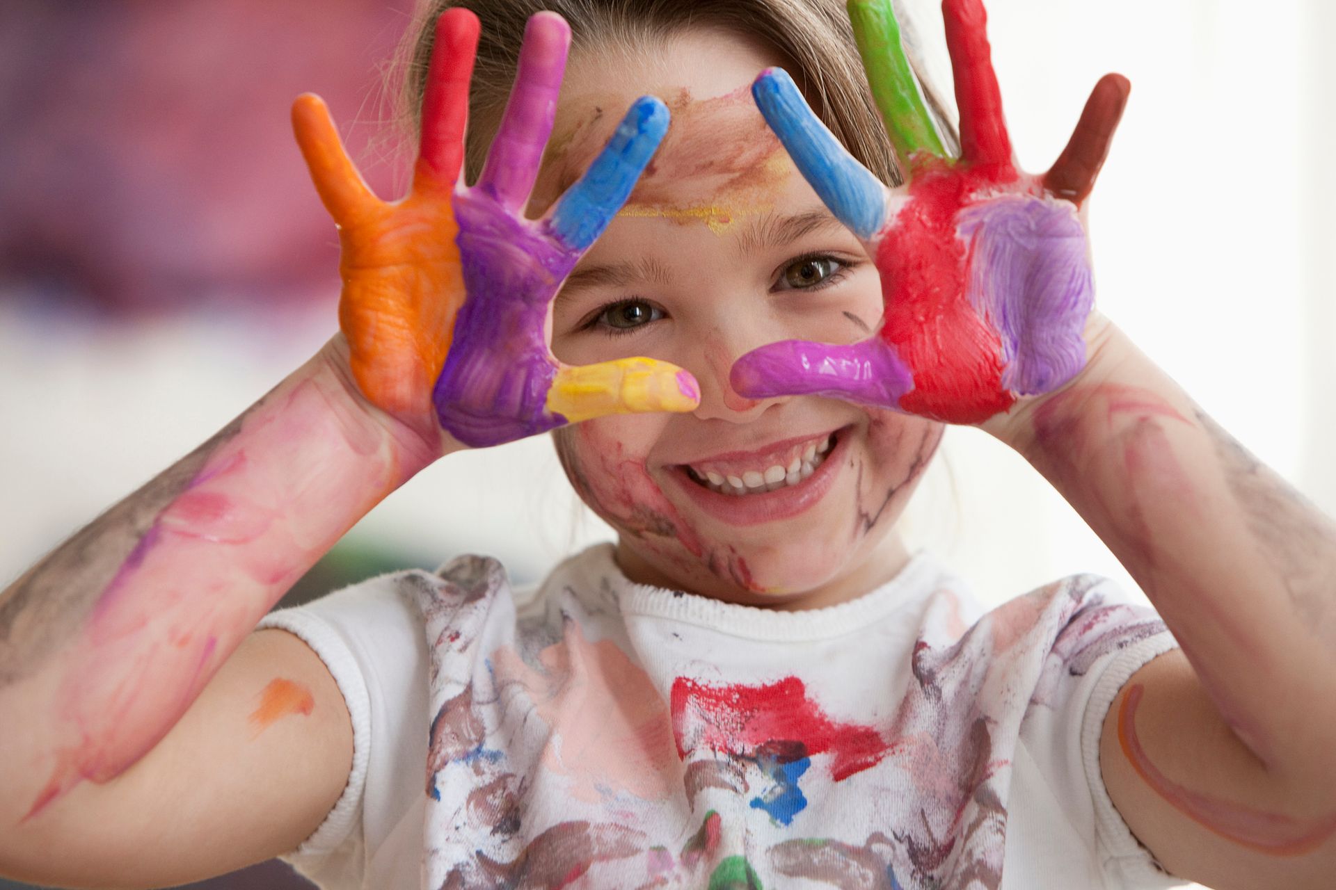 Girl with colorful painted hands, smiling, some paint on her face and shirt.