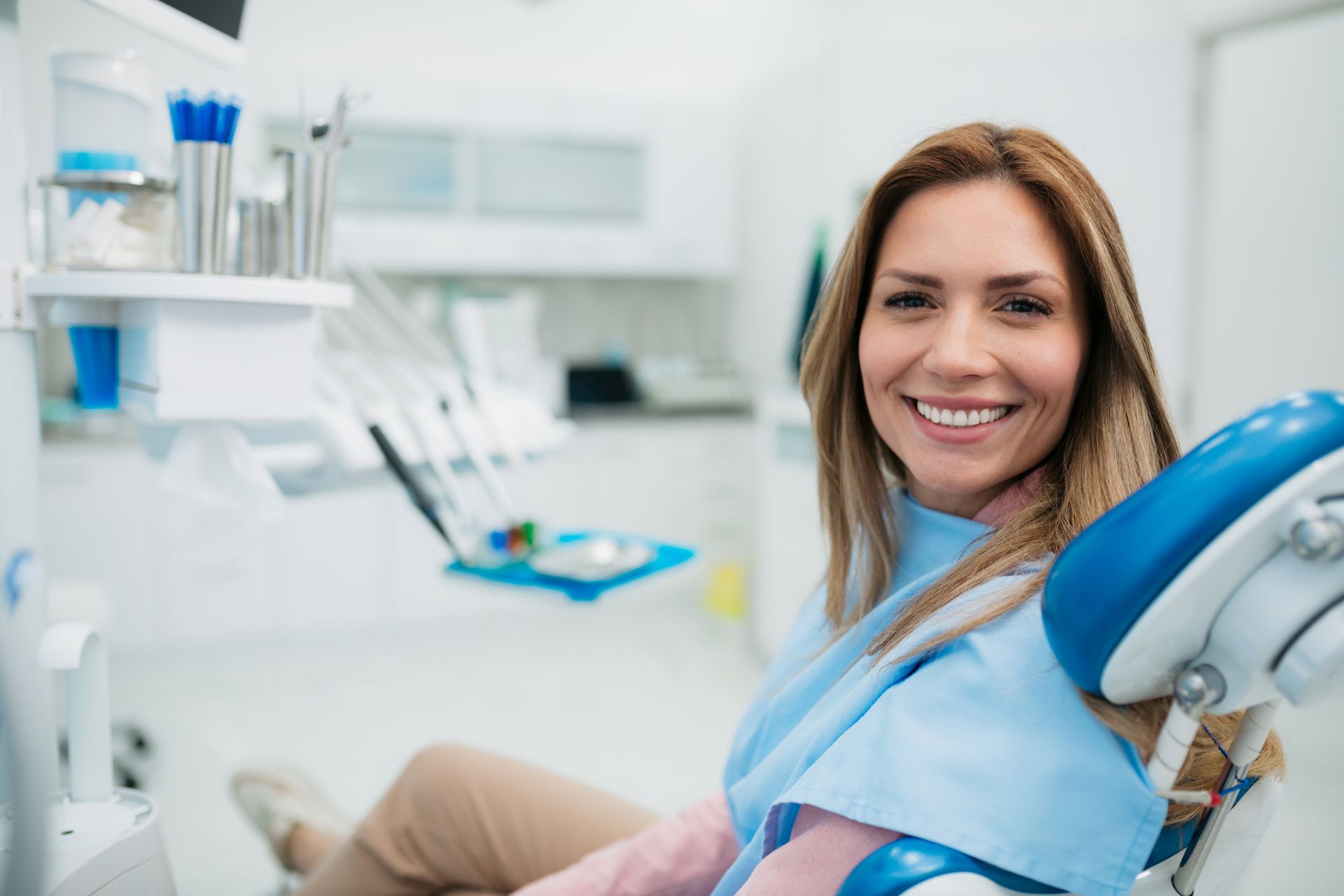 Woman in dentist chair, smiling. Bright dental office setting.
