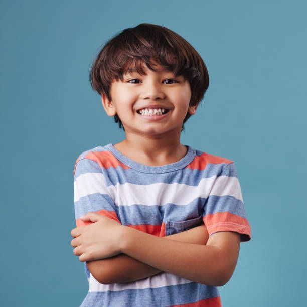 Young boy with brown hair and a big smile, arms crossed, wearing a striped shirt, on a blue background.
