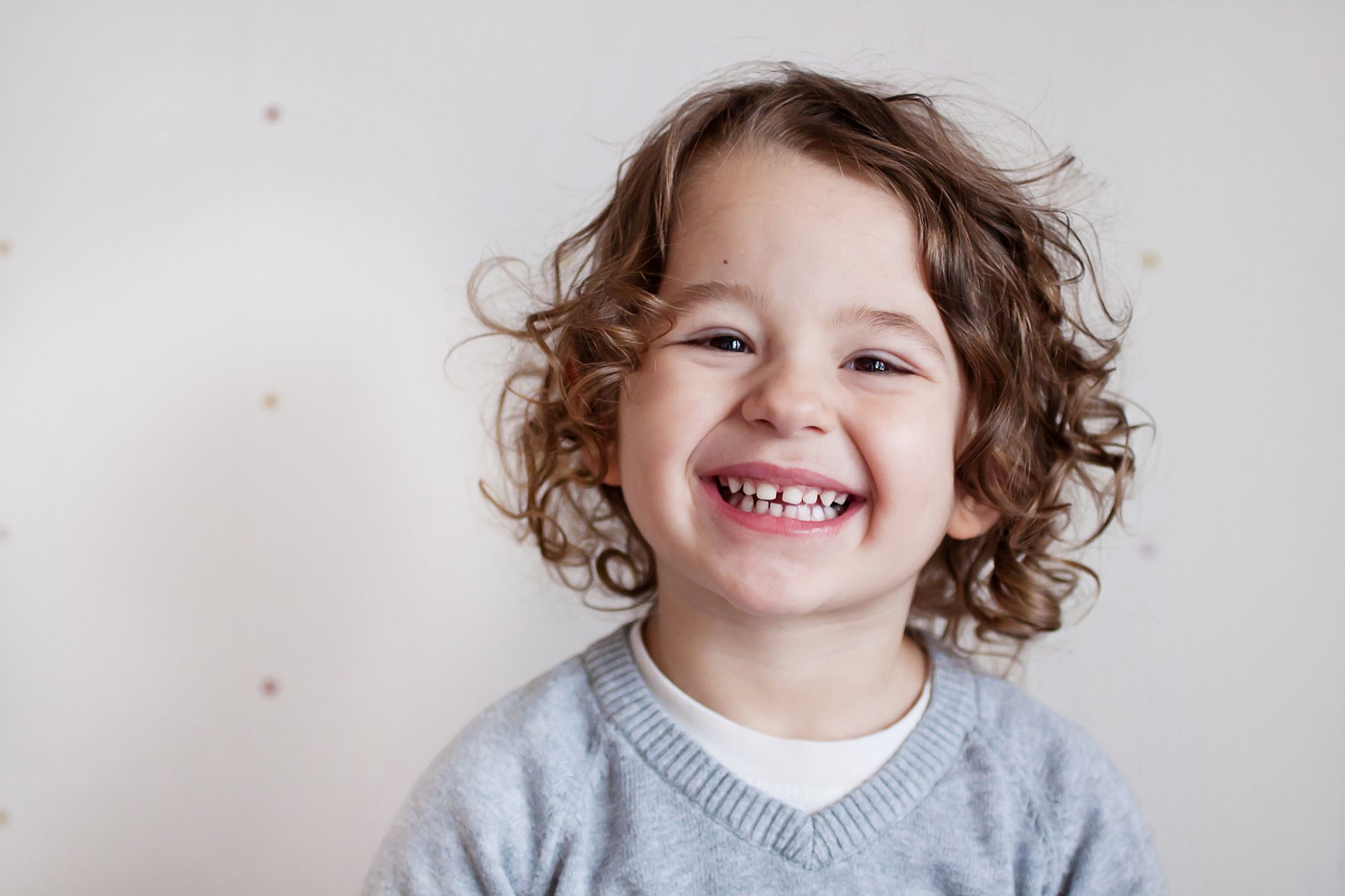 Smiling child with curly brown hair, wearing a blue sweater, against a white background.
