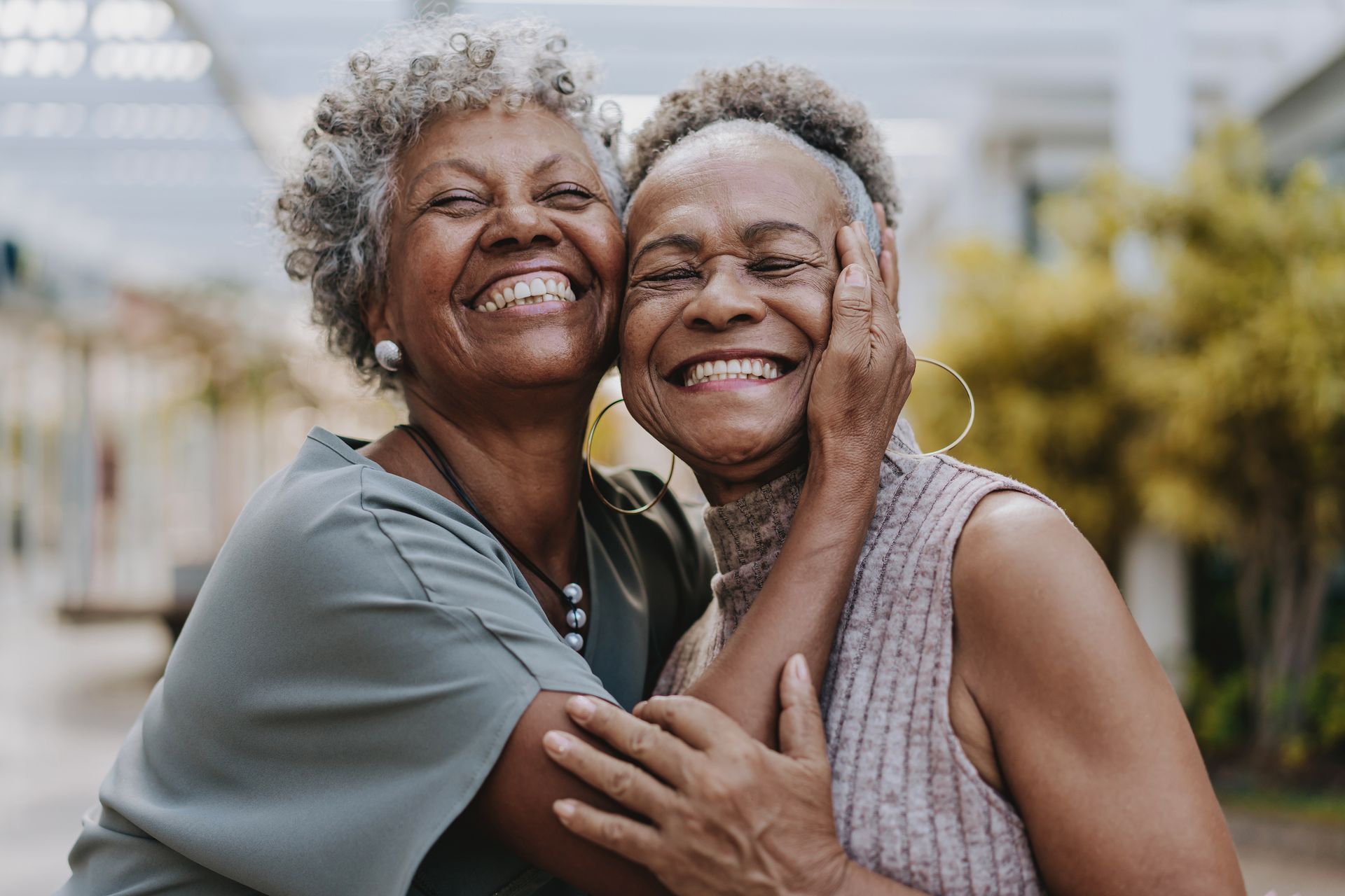 Two older Black women embracing and smiling outdoors.