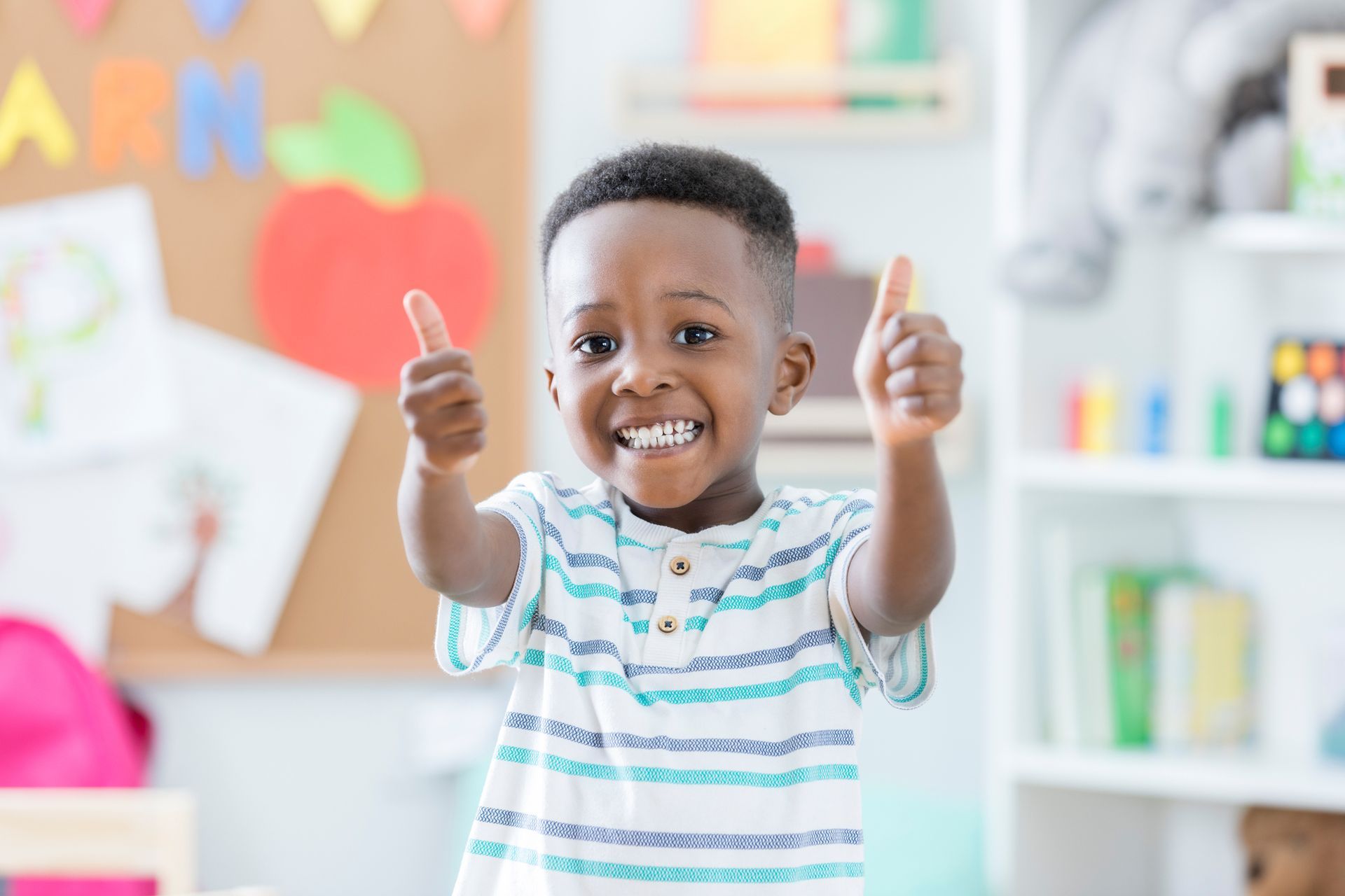 Smiling Black child in a classroom gives thumbs up, excited.