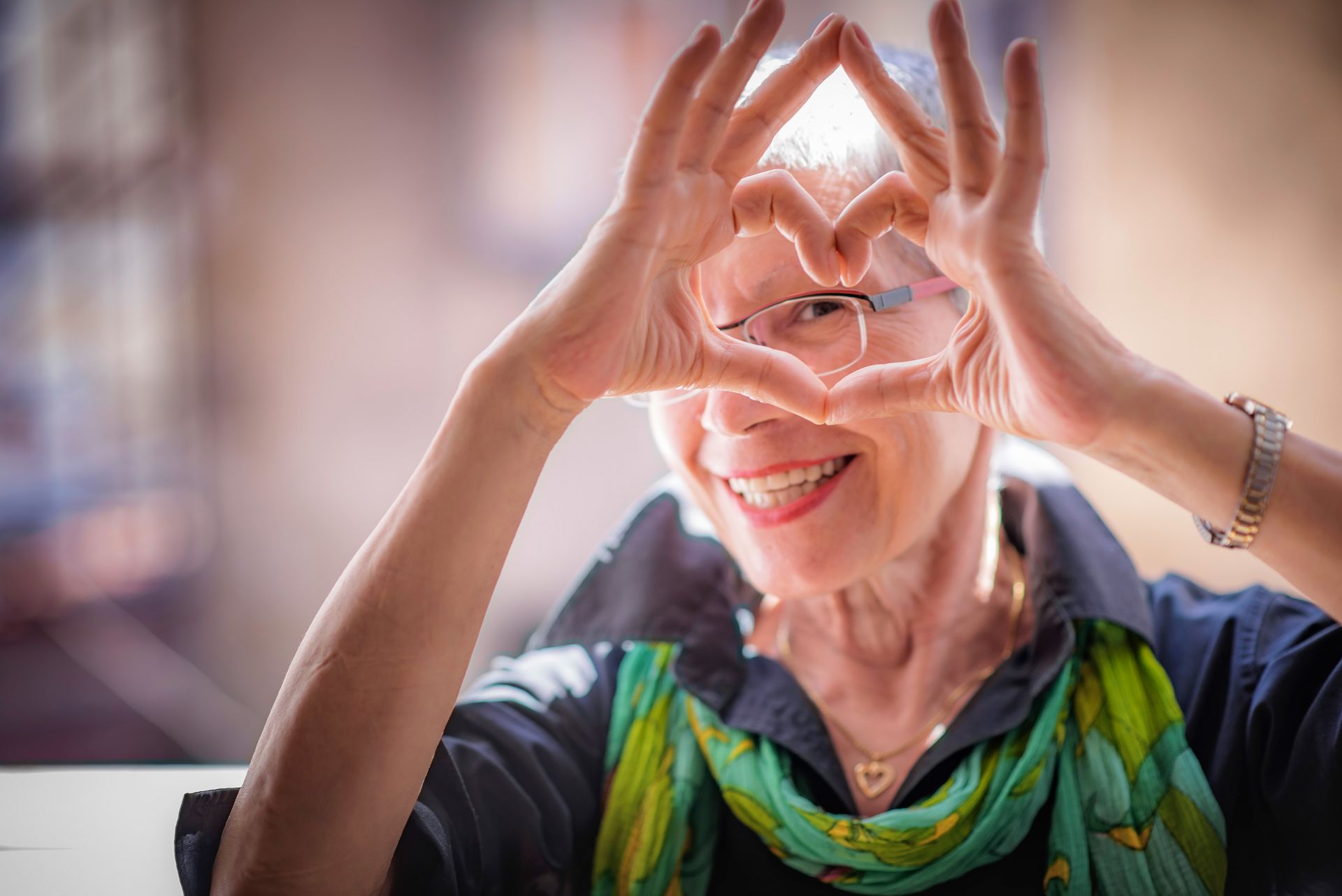 Smiling older woman making a heart shape with her hands, looking through it.