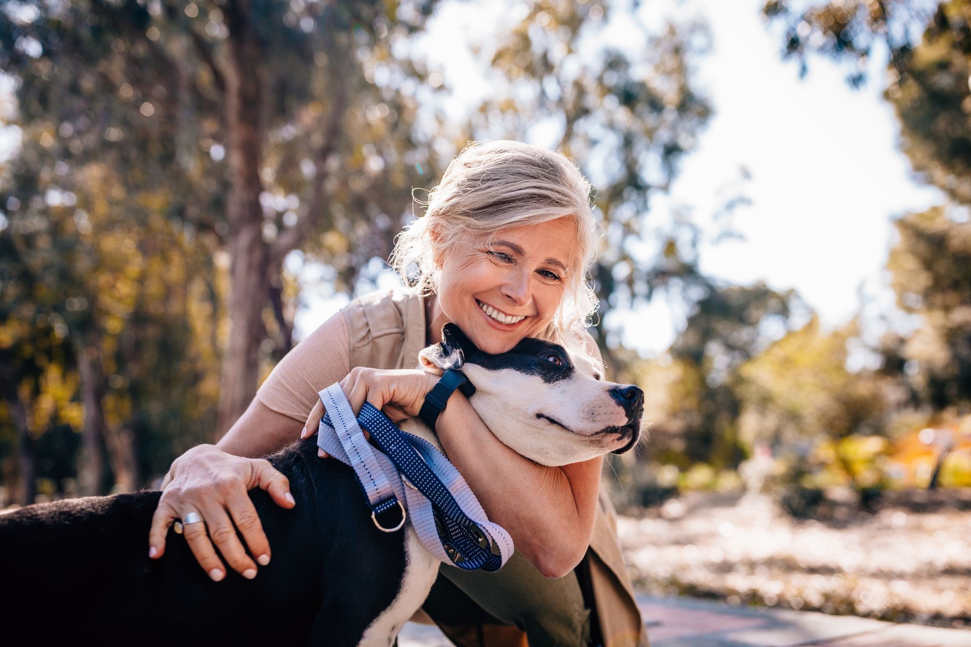 Woman smiling, hugging a black and white dog outdoors.