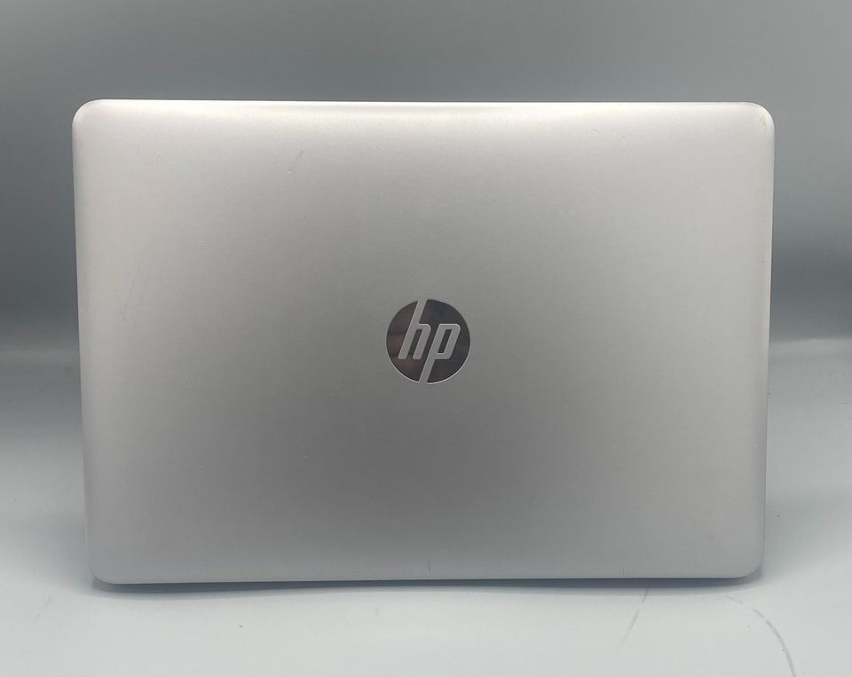 Silver HP laptop, open with a blue abstract wallpaper on the screen. The keyboard and touchpad are visible.