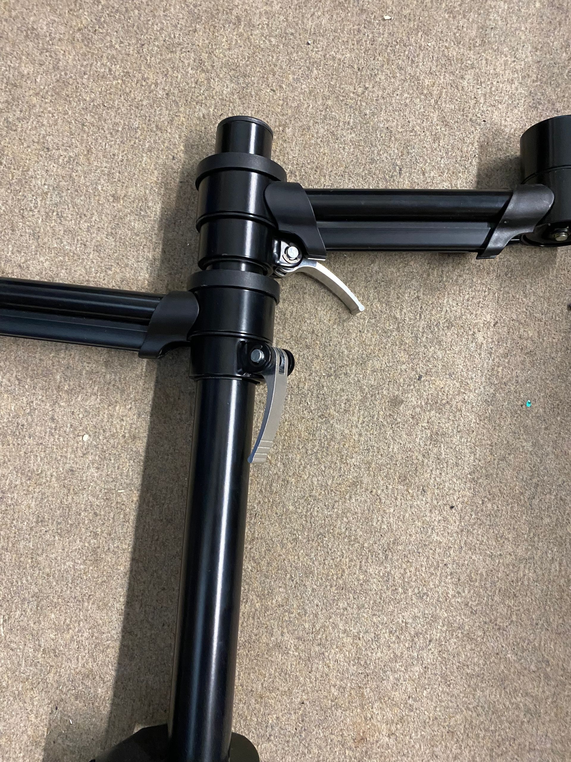 Black dual monitor arm on beige carpet, clamped to a desk.