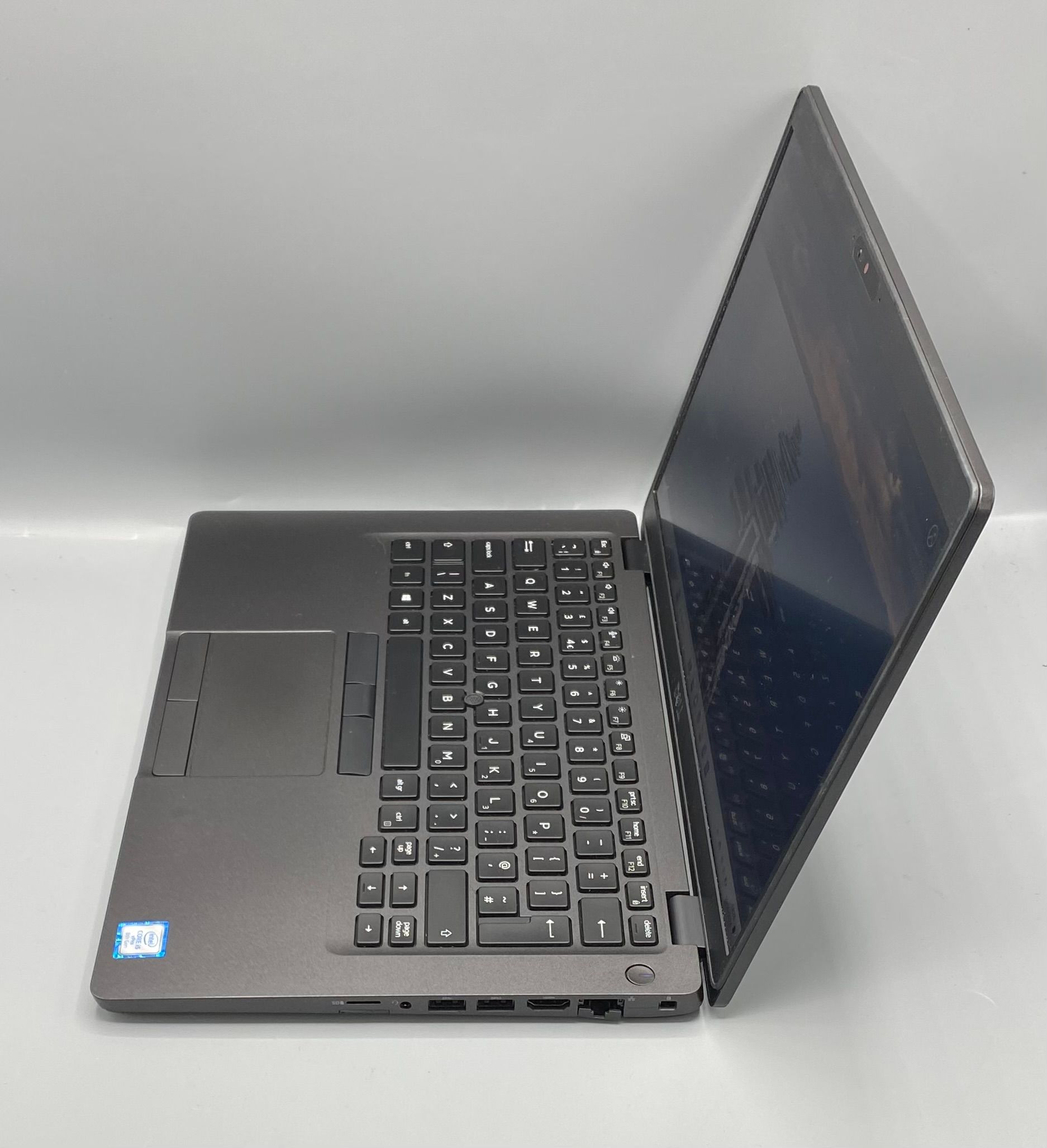 A Dell laptop open on a white surface, displaying a dock scene. Gray exterior, black keyboard.