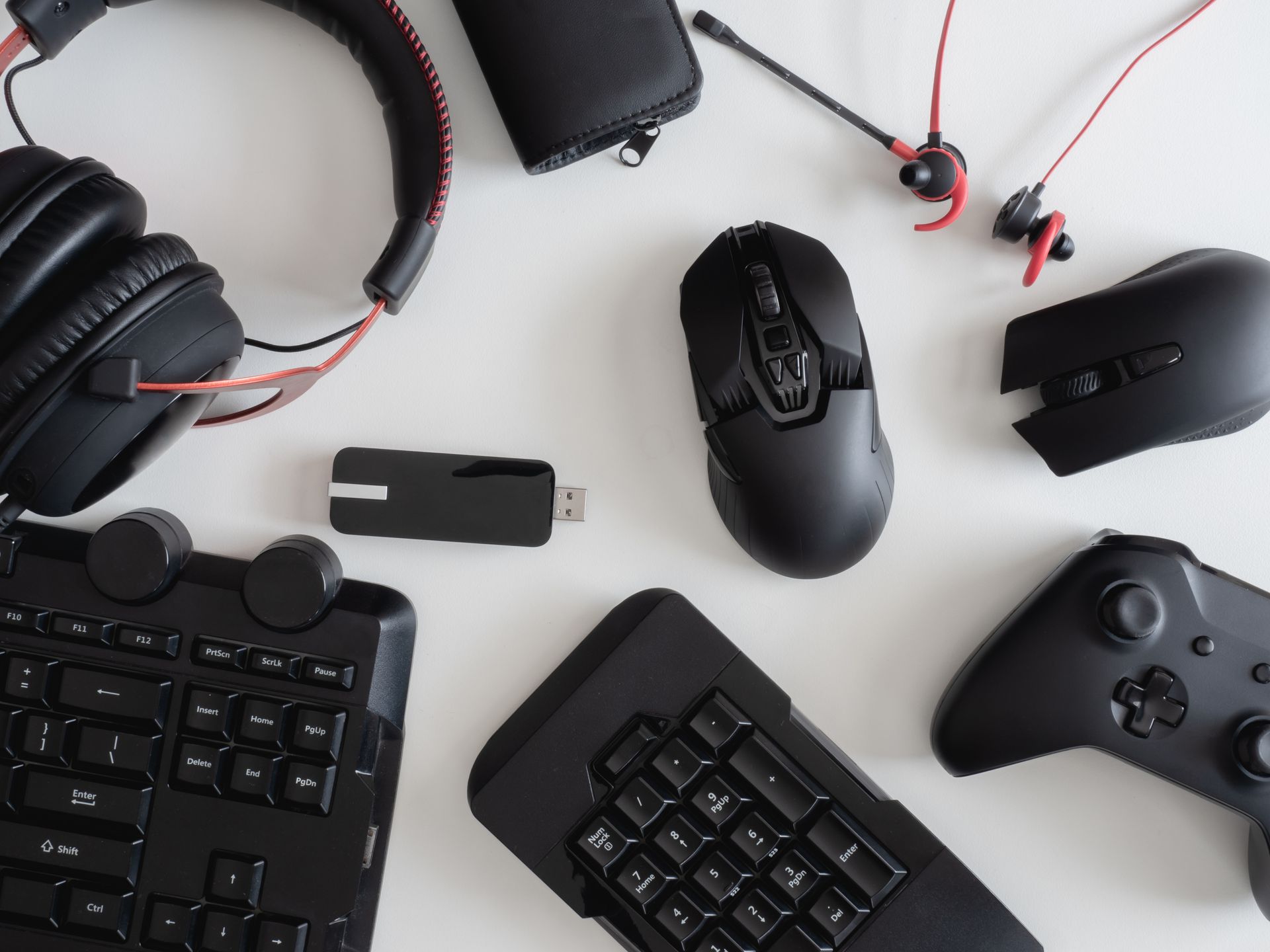 Black gaming accessories on a white surface: headphones, mouse, keyboard, gamepad, and earbuds.
