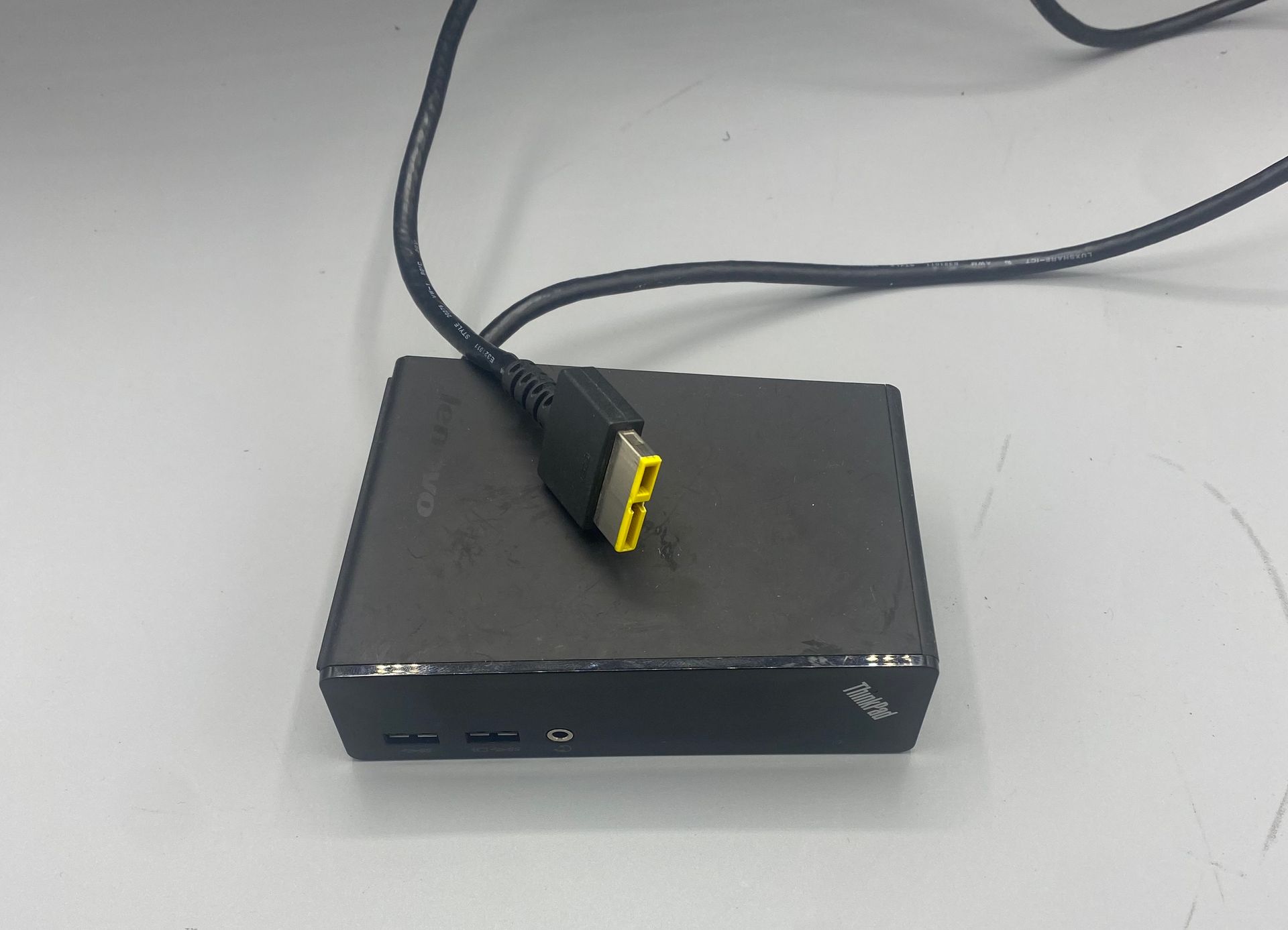 A small black Lenovo ThinkCentre computer on a white surface, connected to a black cable.