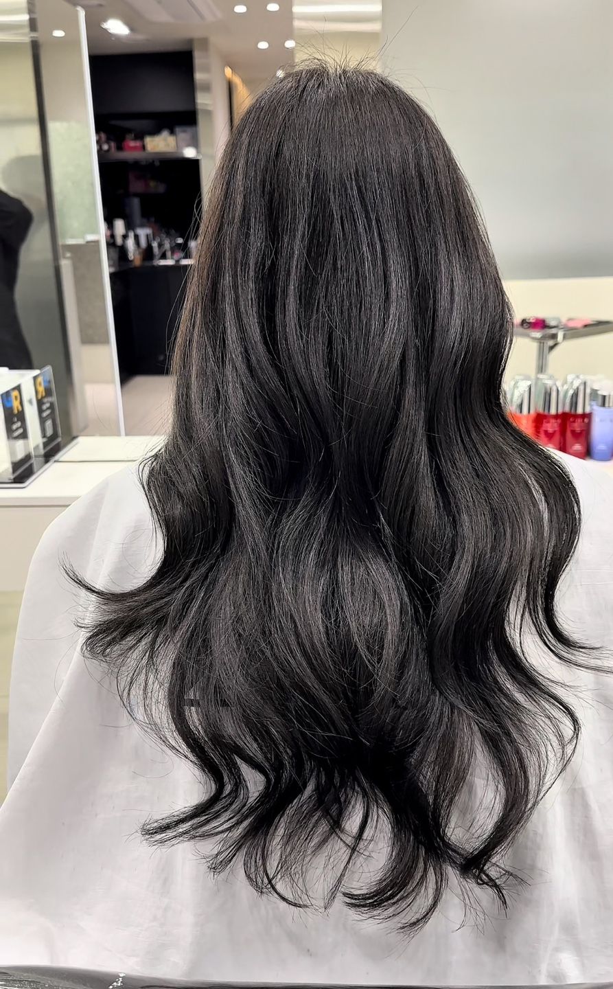 A woman with long black hair is sitting in a chair in a salon.