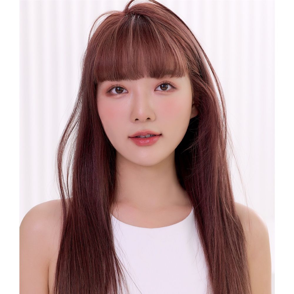 A woman with long brown hair and bangs is wearing a white tank top.