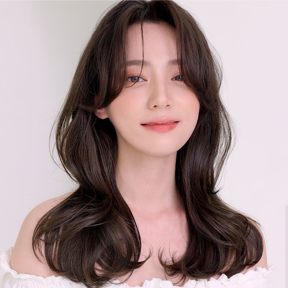 A woman with long brown hair is wearing a white off the shoulder top.