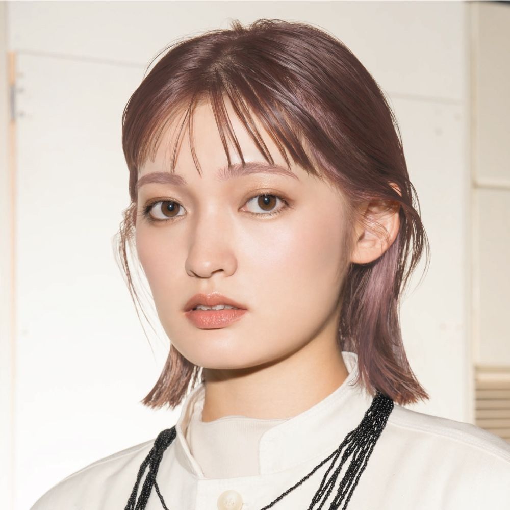 A woman with pink hair is wearing a white shirt and a black necklace