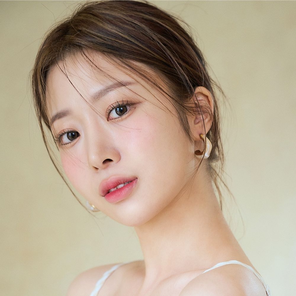 A close up of a woman 's face wearing a white tank top and earrings.