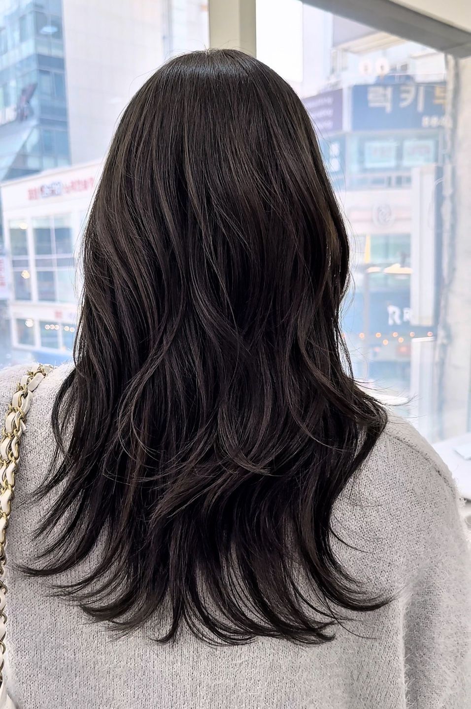 A woman with long black hair is standing in front of a window.