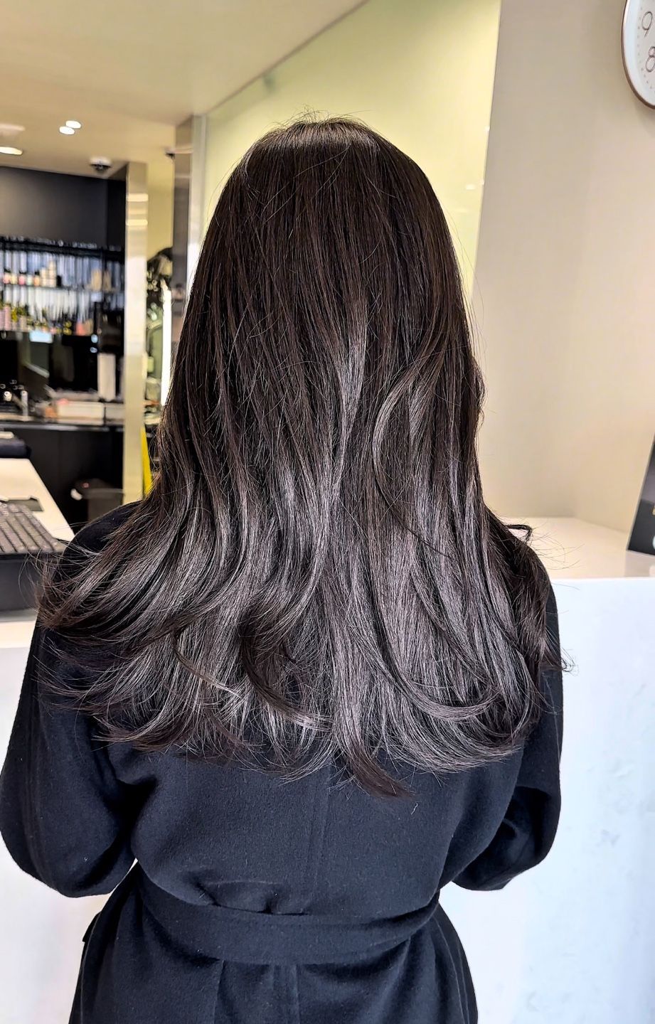 A woman with long black hair is standing in a salon.