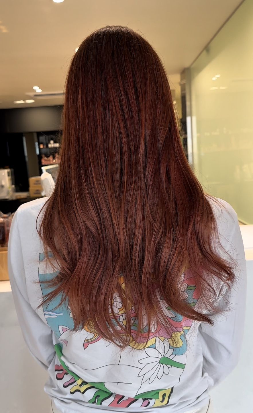 A woman with long red hair is wearing a white sweatshirt.