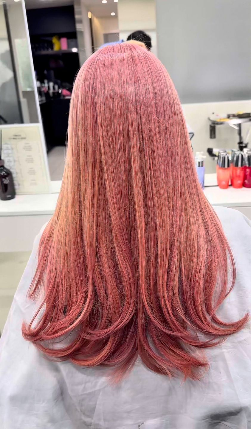 A woman with long pink hair is sitting in a chair in front of a mirror.