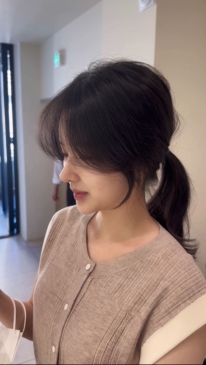 A woman with long hair is wearing a sweater and a ponytail.