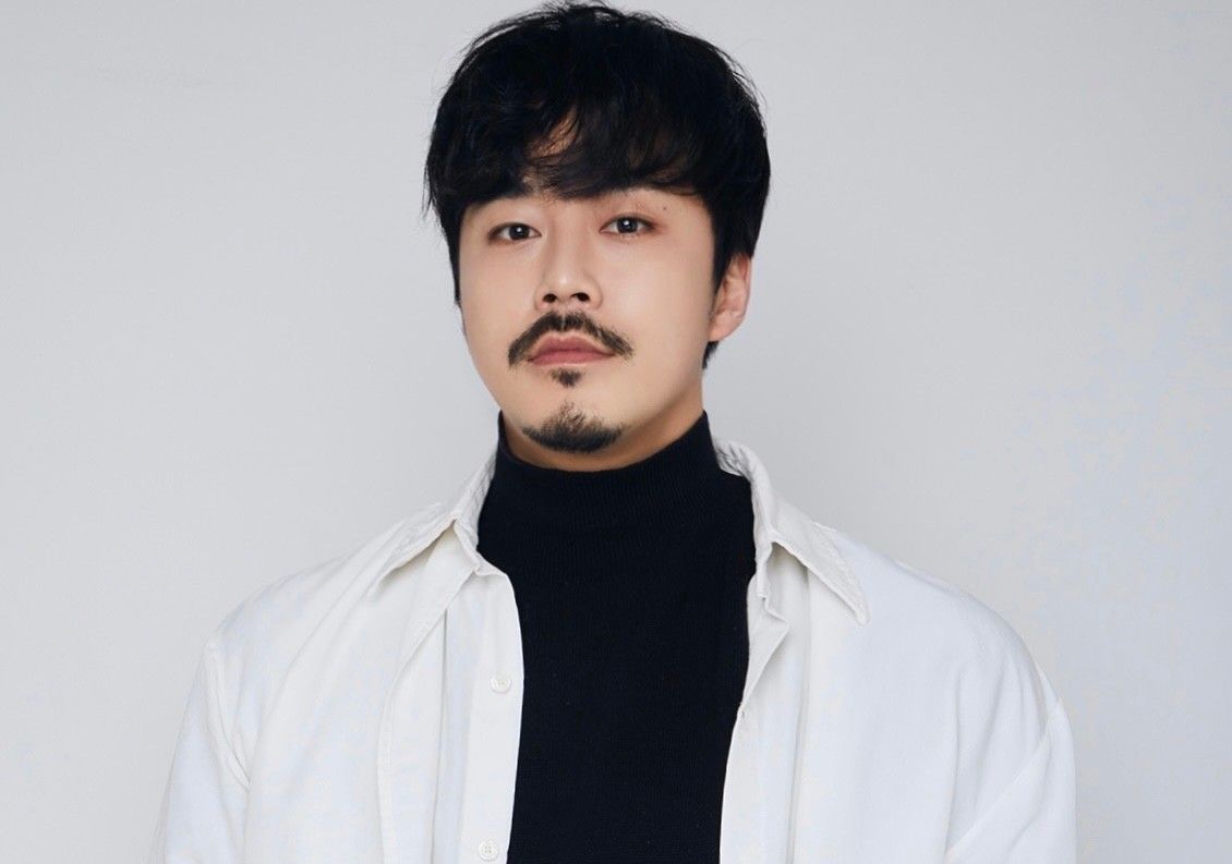 A man with a beard is wearing a white shirt and a black turtleneck.