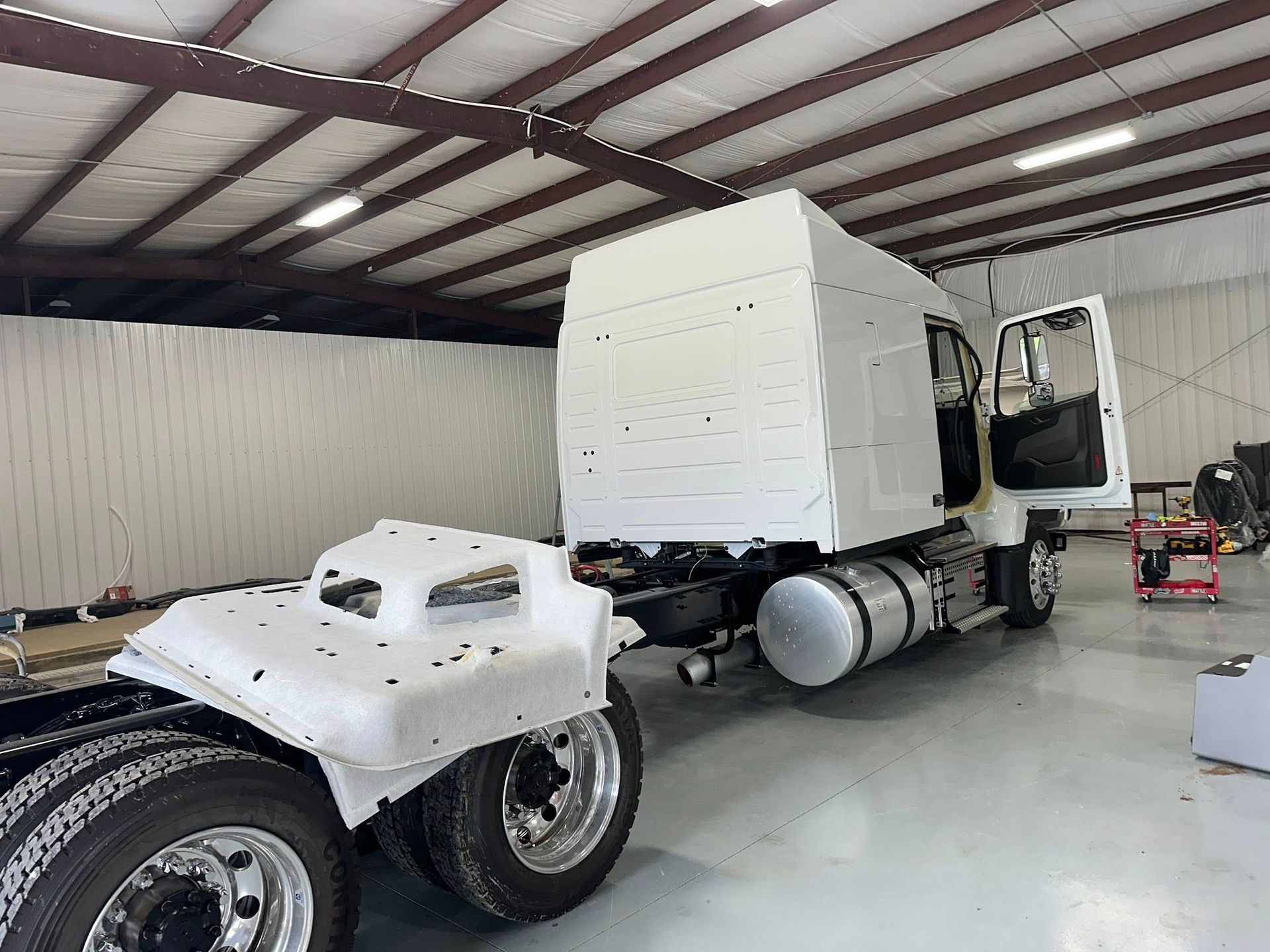 White semi-truck cab in a warehouse; the cab is mounted on the chassis, with the door open.