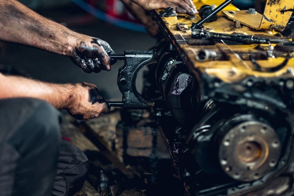 Hands Covered in Grease Working on A Disassembled Yellow and Black Engine — SAE Engineering in Mount Sheridan, QLD