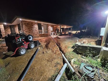 Nighttime Construction Scene. a Mini Excavator Digs a Trench Near a Brick House — SAE Engineering in Tablelands, QLD