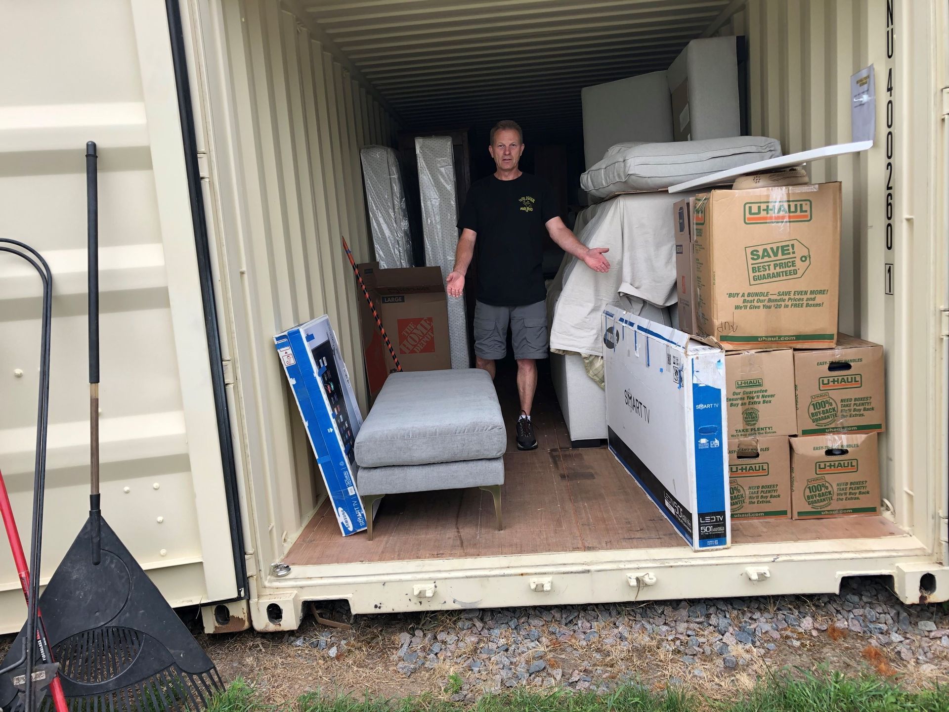 Man standing inside a storage container filled with furniture and boxes.