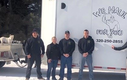 Four people stand in front of a moving truck with 
