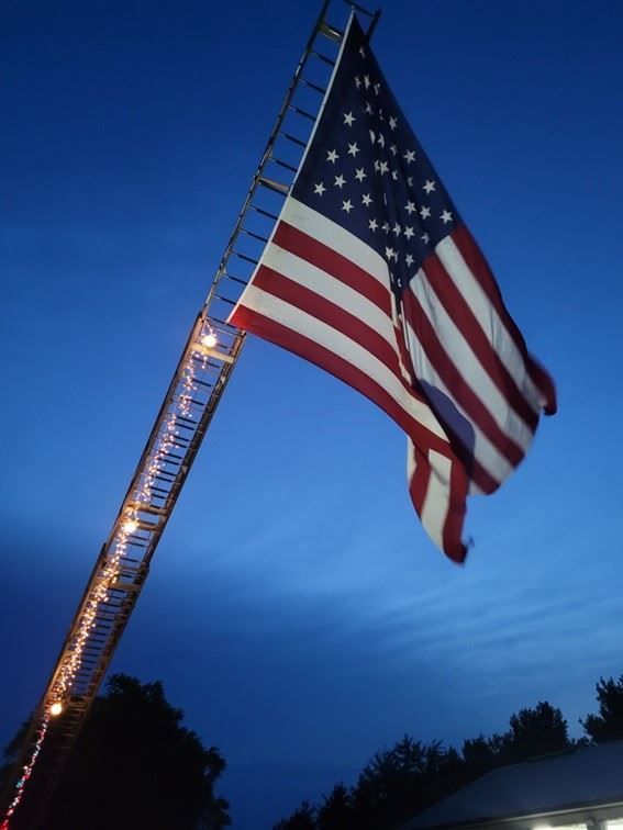 American flag on a fire truck ladder against a dark blue evening sky.