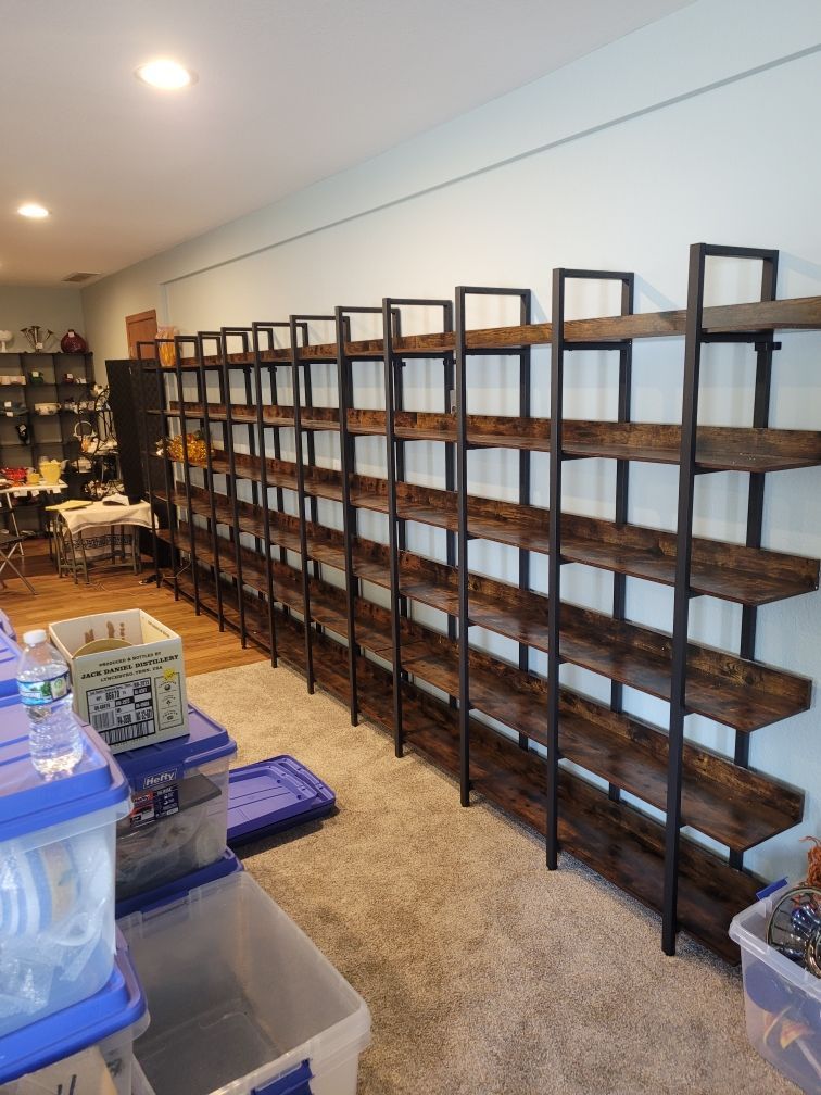 Long, dark wooden shelves with black metal frames line a wall in a room with carpet and plastic storage bins.