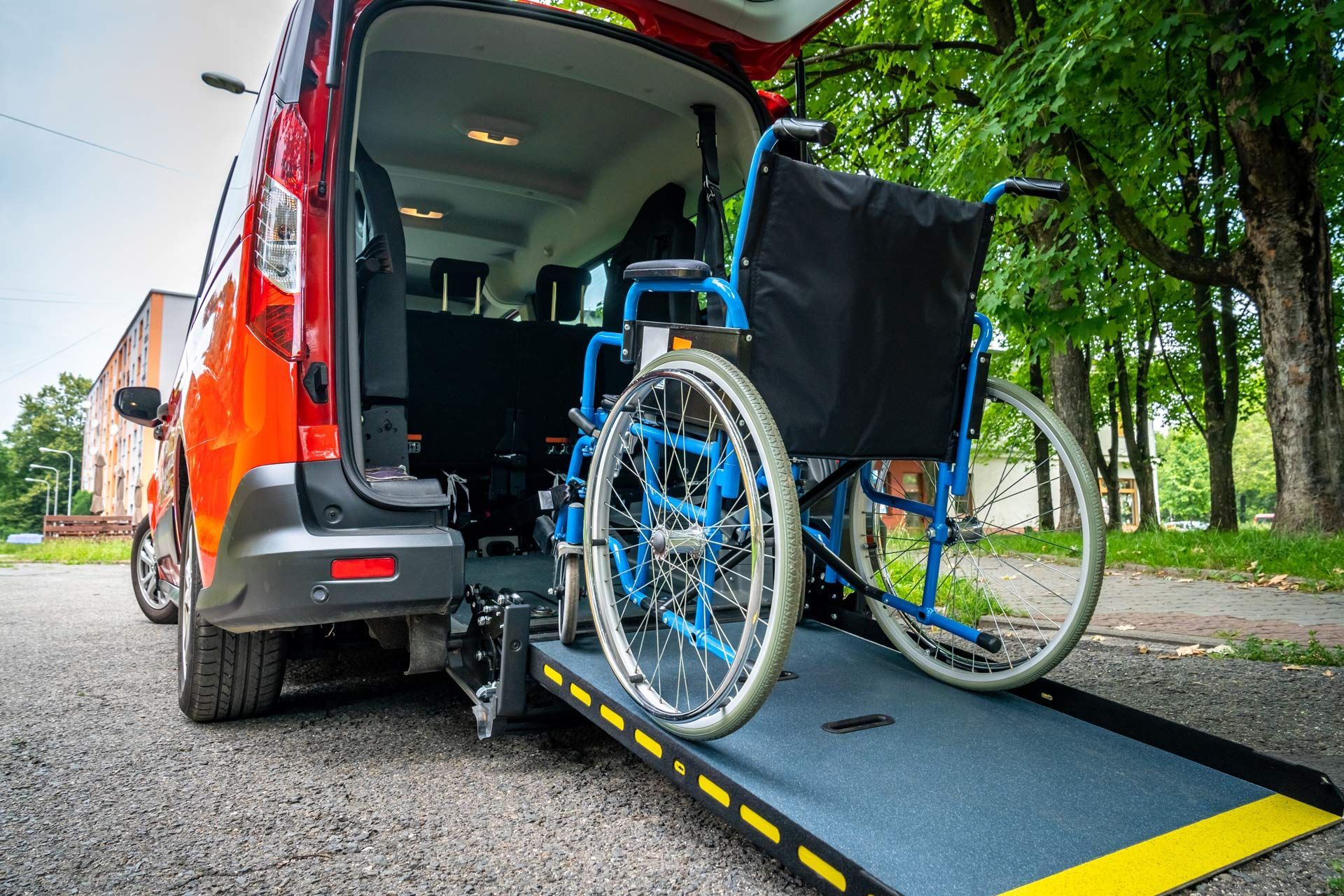 A wheelchair sits on a ramp extending from the open back of a red van.